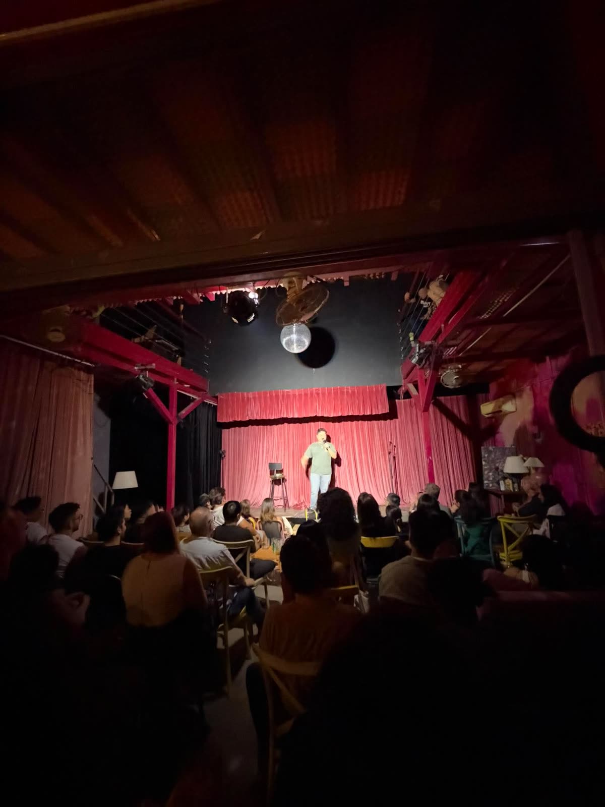 The full Shout Bar crowd seen from the back of the room, facing the red-curtained stage