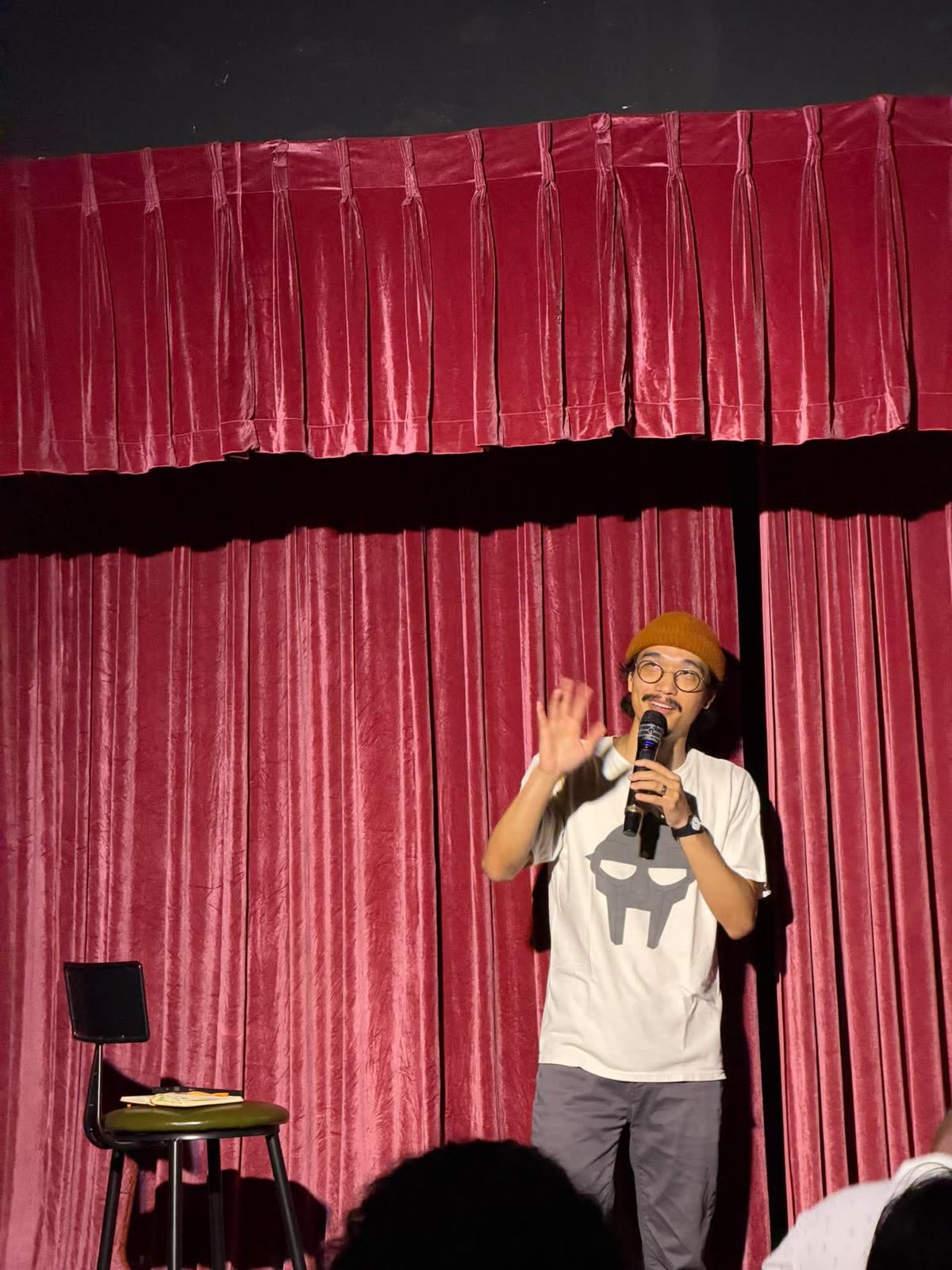 Host Matt Tran in a beanie, hand raised, on stage at Shout Bar